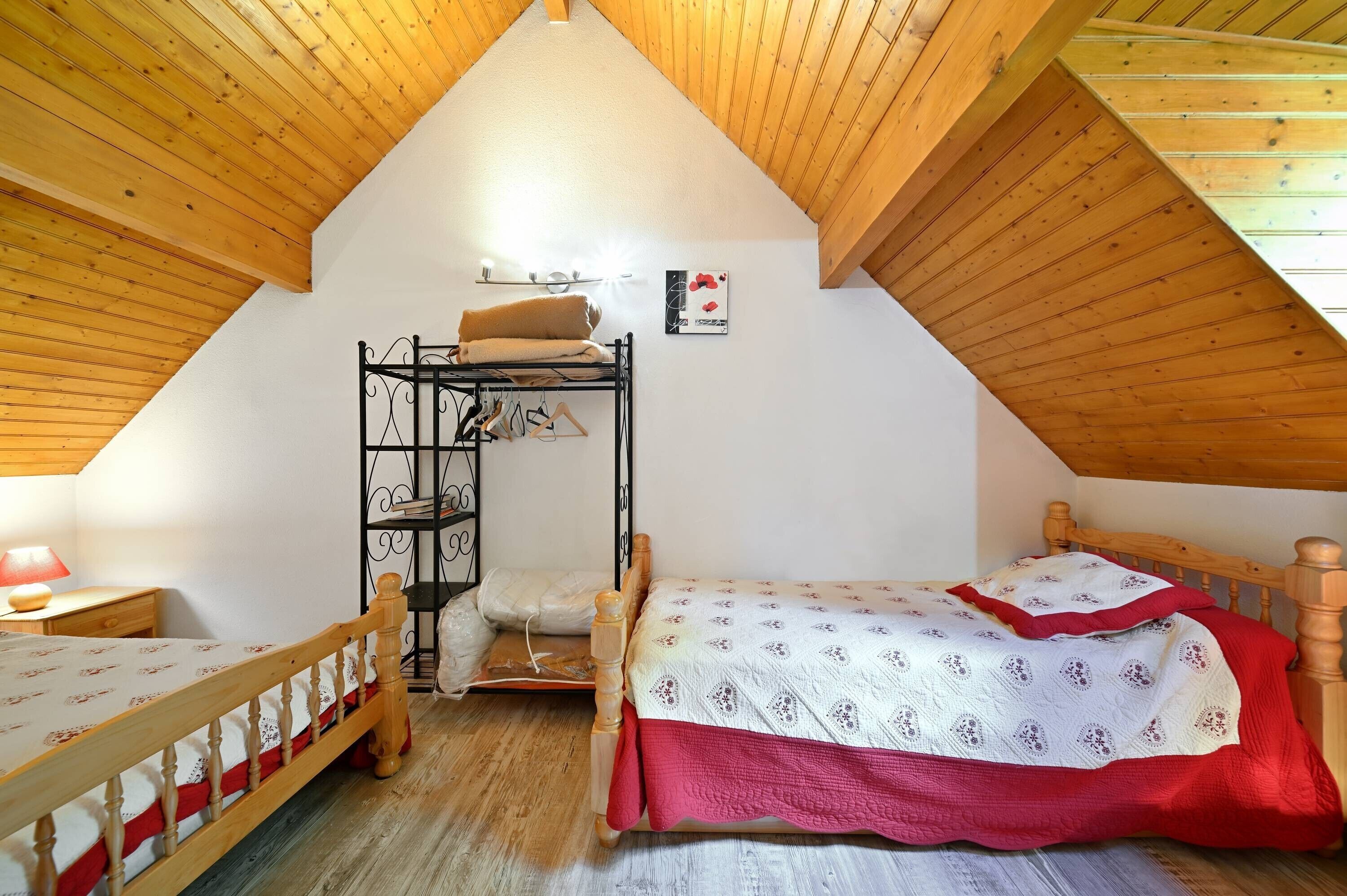 Une chambre mansardée chaleureuse avec des poutres apparentes, un lit superposé, une table de chevet et une étagère fixée au mur.