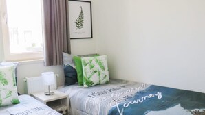 Una camera da letto con due letti, un quadro con felci appeso al muro e una finestra con tende.