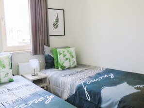 Una camera da letto con due letti, un quadro con felci appeso al muro e una finestra con tende.