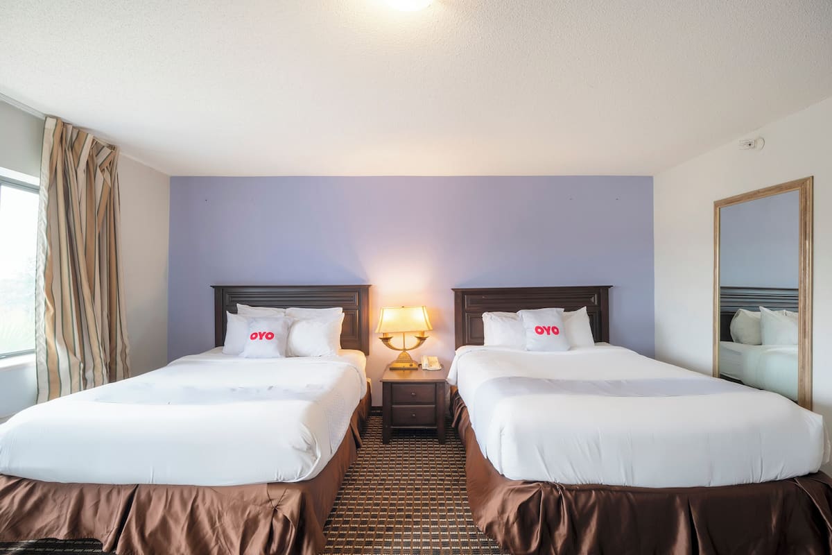 Quarto de hotel com duas camas, uma mesa de cabeceira com abajur e um espelho na parede.