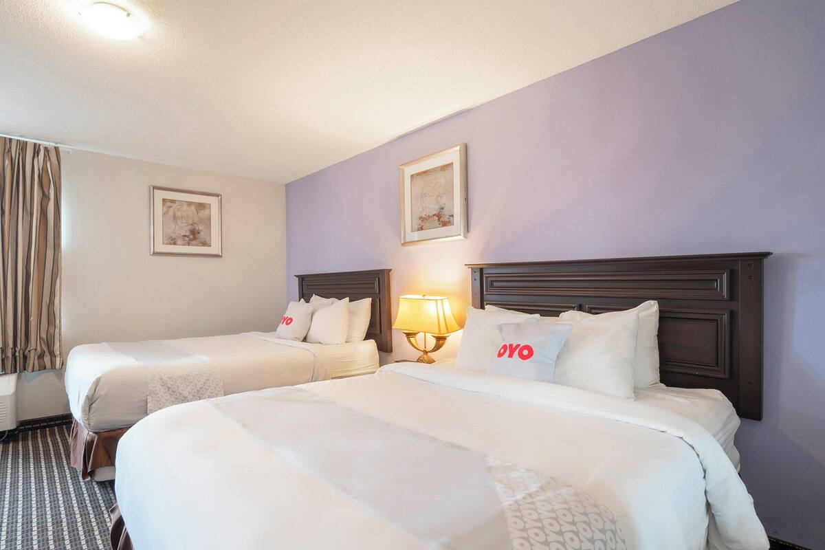 Quarto de hotel com duas camas, uma mesa de cabeceira com abajur e uma janela com cortinas.