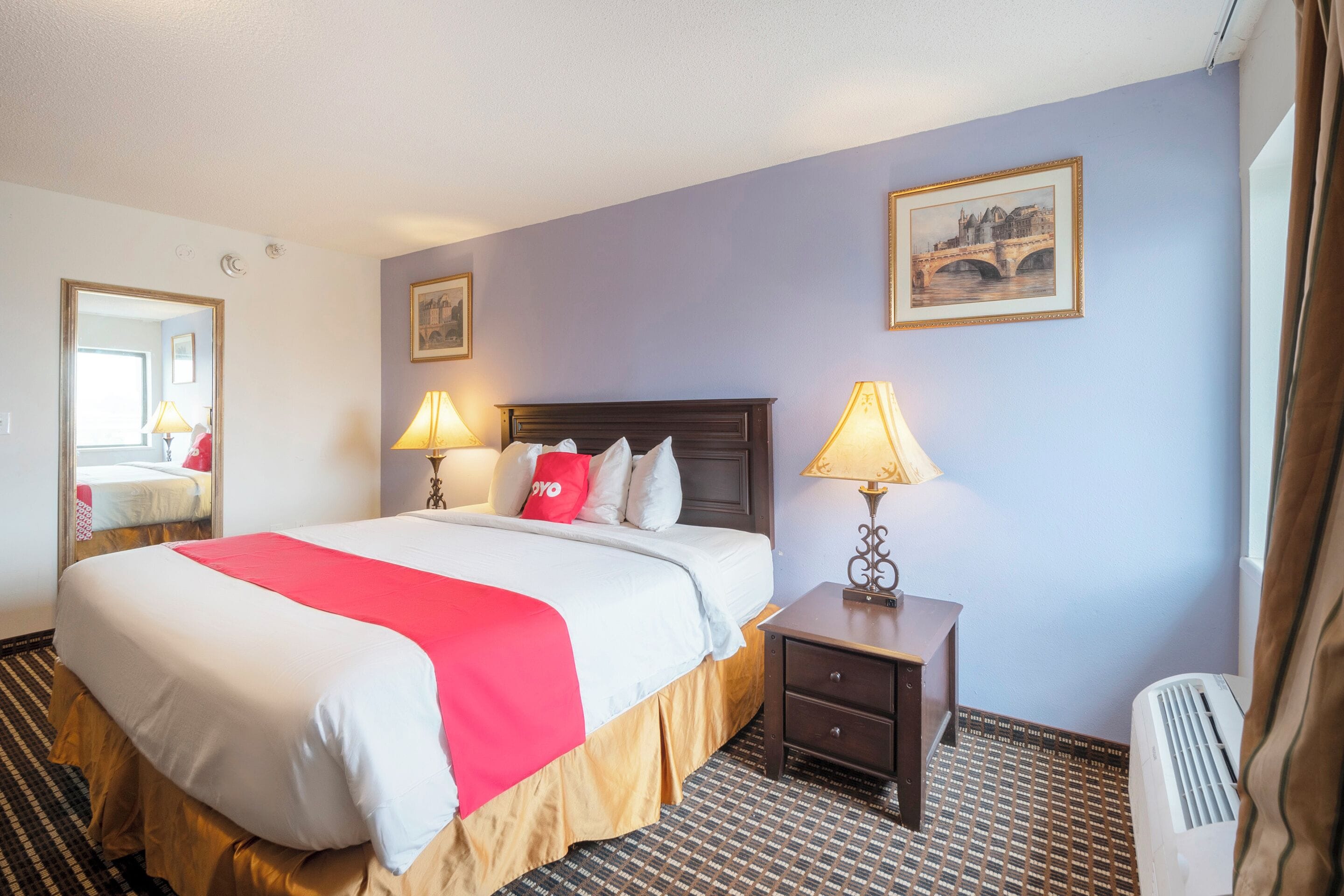 A hotel room with a large bed, two bedside lamps, a nightstand, a framed picture on the wall, and a window with curtains.