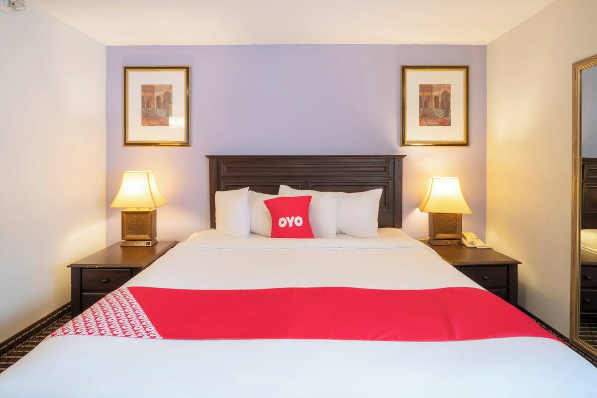 Quarto de hotel com uma cama grande, duas mesas de cabeceira com luminárias e duas fotos emolduradas nas paredes.