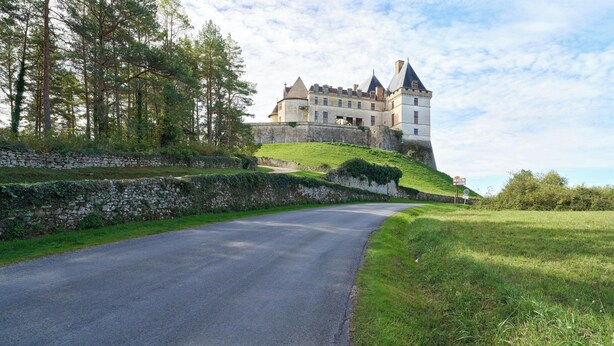Un château perché sur une colline, accessible par une route pavée.