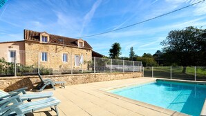 Une piscine avec des chaises longues, un bâtiment en pierre et une cour clôturée.