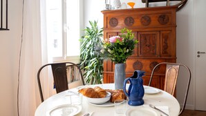 A dining table with plates, a vase with flowers, a pitcher, and a croissant.