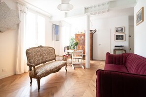 A living room with a wooden herringbone floor, a vintage sofa, a modern red sofa, and a dining area with a white table and chairs. - Appartement Ottomane - Welkeys (Paris)