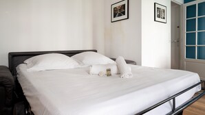 A neatly made bed with white linens, a small bottle, and a rolled towel on the bed.