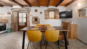 A dining area with a wooden table, yellow chairs, stone walls, a fireplace, and a TV mounted on the wall.