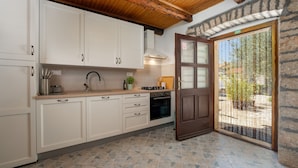 A kitchen with white cabinets, a wooden ceiling, and a stone wall.