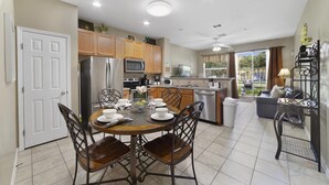 A modern kitchen with wooden cabinets, stainless steel appliances, and a dining area with a round table and chairs.