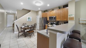 A kitchen with wooden cabinets, a stainless steel refrigerator, a microwave, and a stove. There is a dining table with chairs and a kitchen island with stools.