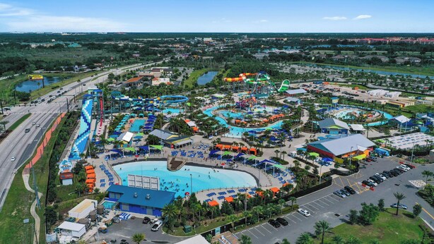 An aerial view of a water park with multiple pools, slides, and a large parking area.