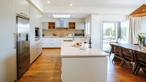 A modern kitchen with a central island, stainless steel appliances, and wooden flooring. - Penshurst - Lake Views - Sleeps 8 (Wanaka)
