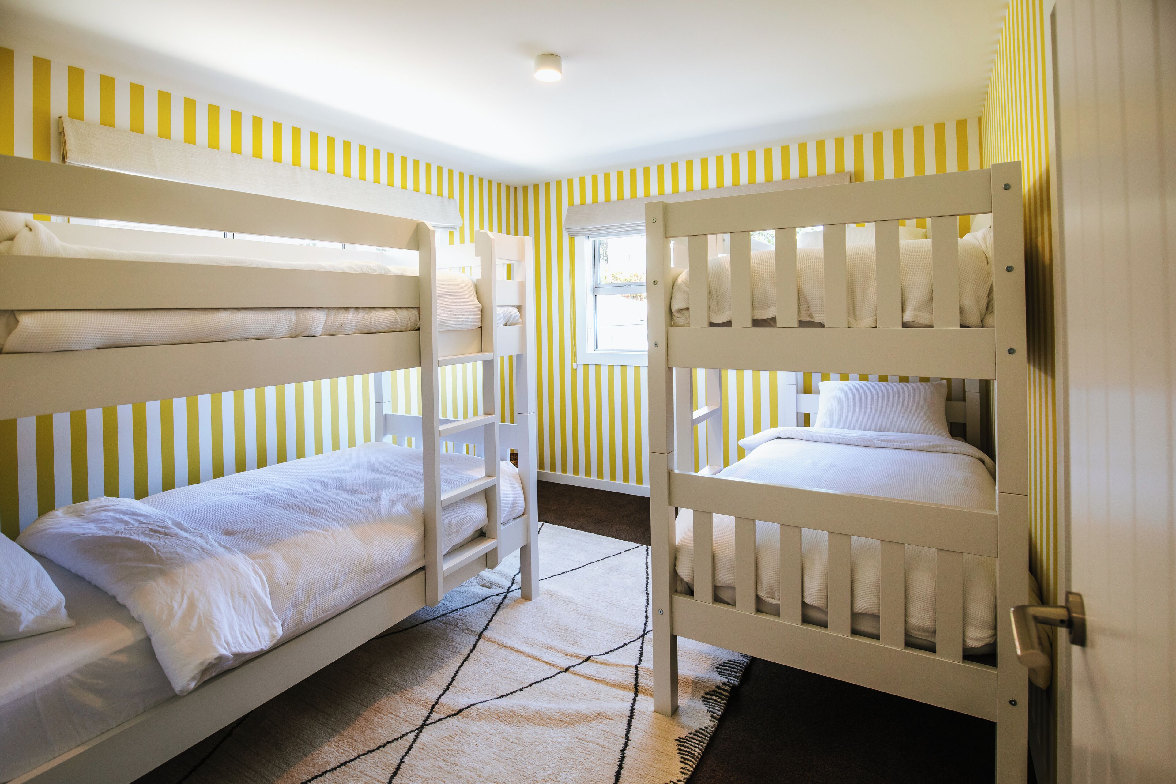 Een kamer met twee stapelbedden, een raam en gestreept behang.