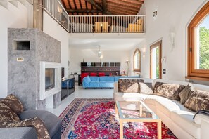 Un amplio salón con chimenea, un sofá grande, una mesa de centro y un tapete rojo estampado.