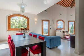 A dining area with a table, red chairs, and a blue sofa. There are windows with views of greenery. - Villa 'Serafina' with Private Pool and Private Terrace (Pescia)
