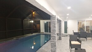 An indoor swimming pool with a glass enclosure, stone pillars, and a seating area with wicker chairs.
