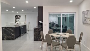 A modern kitchen with a marble countertop and a dining area with a glass table and chairs.