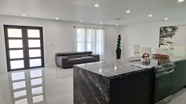 A modern kitchen with a marble island, a built-in oven, and a seating area with a sofa.