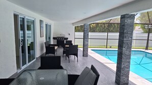An outdoor patio area with a pool, black wicker furniture, and a grill.