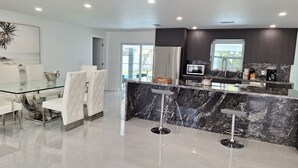 A modern kitchen with a marble countertop, stainless steel appliances, and a glass dining area with white chairs.