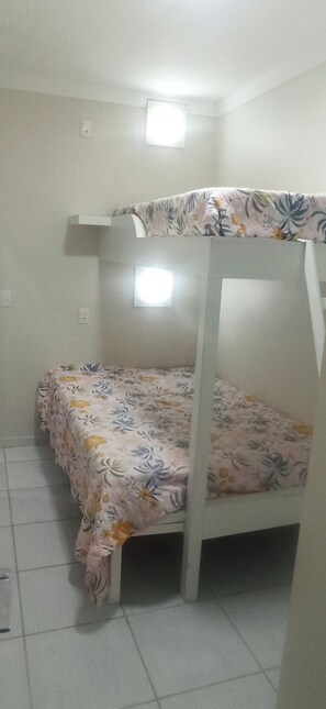 Ein Stockbett mit Blumenmuster-Bettwäsche in einem Zimmer mit weißen Wänden und Fliesenboden.