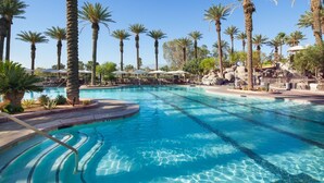 Ein Swimmingpool mit klarem, blauem Wasser, umgeben von Palmen und Liegestühlen.