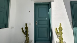 Une porte de couleur bleu-vert, un mur blanc et une petite fenêtre sur la gauche.