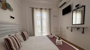 Une chambre d’hôtel avec un grand lit, une table de chevet avec des serviettes, une chaise, un téléviseur et une fenêtre avec des rideaux.