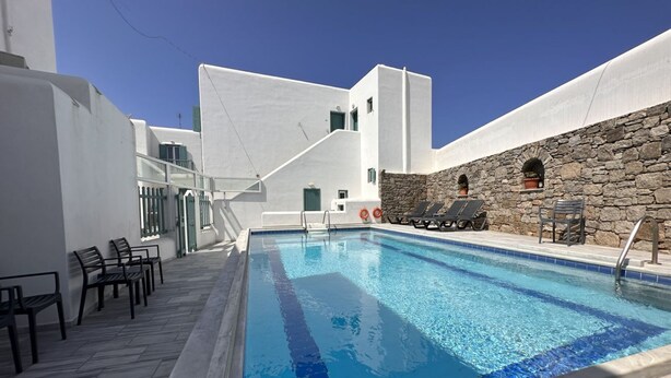 Une piscine bordée d’un mur en pierre et un bâtiment blanc avec un escalier.