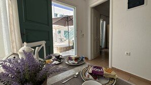 Un coin repas avec une table dressée pour deux personnes, une plante en pot et une vue sur le balcon extérieur.