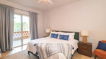 A bedroom with a bed, two bedside tables, a nightstand, a ceiling fan, and a view of a balcony.