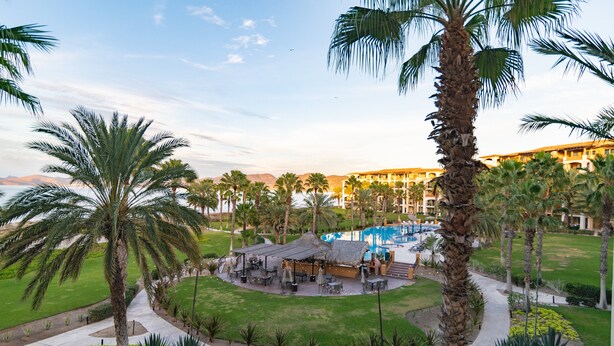 Een resort met een zwembad, palmbomen en een gebouw met meerdere balkons.