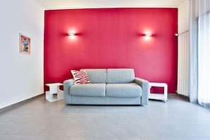 A modern living room with a grey sofa, a red accent wall, and two white side tables.