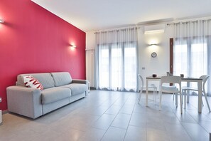 Un salon moderne avec un canapé gris, une table à manger avec des chaises et un mur d’accent rouge.