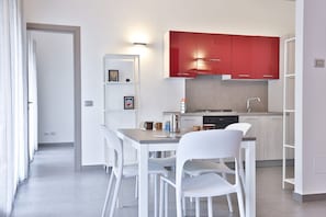 Une cuisine moderne avec des meubles blancs et rouges, une table à manger avec des chaises et un petit îlot central doté d’une machine à café.