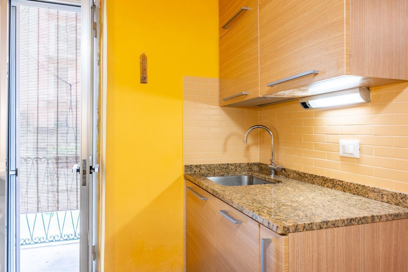 Une cuisine dotée d’un plan de travail en granit, d’un évier en acier inoxydable, de meubles en bois et d’une fenêtre visible, pourvue de stores.