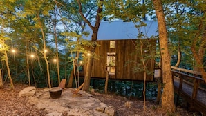 A wooden cabin surrounded by trees with a stone pathway and a chair.