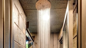 A narrow, wooden-walled shower area with a hanging showerhead, stone walls, and a small plant.