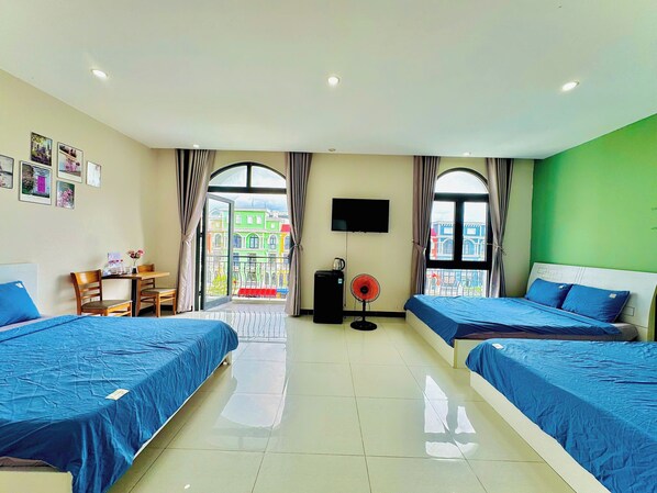 A hotel room with two beds, a dining table, chairs, a TV, and a balcony with a view of colorful buildings. - Haleeda Homestay Grand World Phu Quoc (Phu Quoc)