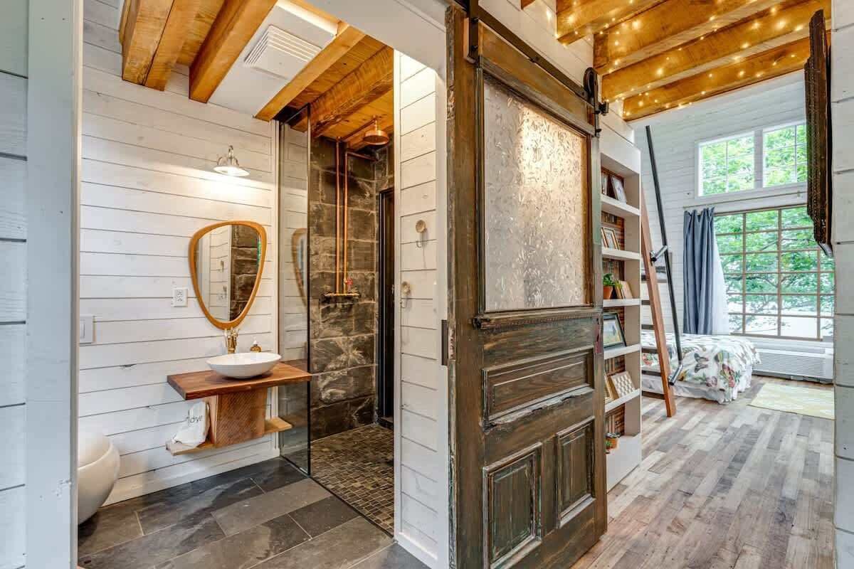 Een rustieke badkamer met een houten wastafelmeubel, een stenen douche en een houten deur met planken.