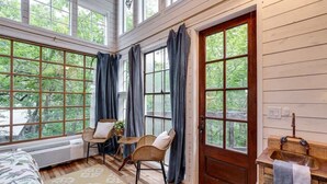 Una habitación con ventanas amplias, una puerta de madera, un lavamanos y una silla.