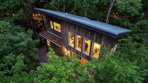 Una cabaña moderna de madera con ventanas amplias, una terraza y rodeada de un bosque denso.