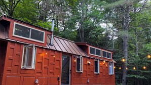 Une cabane en bois rouge avec un toit en métal, un porche à l’avant et une terrasse aménagée avec du mobilier d’extérieur.