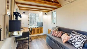Un intérieur moderne avec un escalier en bois, un canapé agrémenté de coussins à motifs et un coin repas comprenant une chaise et une table.