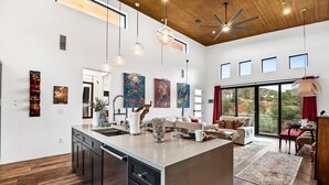 A spacious kitchen with a large island, modern pendant lights, and a view of the outdoors through large windows. - Beautiful Views Of Cathedral Rock, Hot Tub, Fire Pit, Wildlife Sightings, And Stargazing (Sedona)