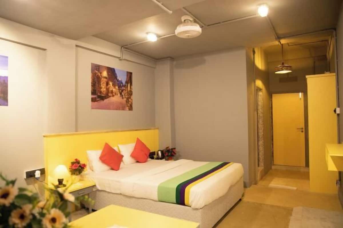 A hotel room with a bed, a nightstand, a lamp, a picture on the wall, and a door leading to another room.