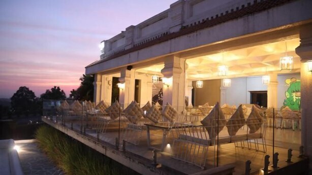 An outdoor seating area with chairs and tables, a stone pathway, and a building with columns and a balcony. - Hotel FORT28 (Nagpur)