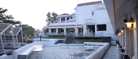 Un patio con piscina, asientos al aire libre y un edificio de varios niveles y balcones.